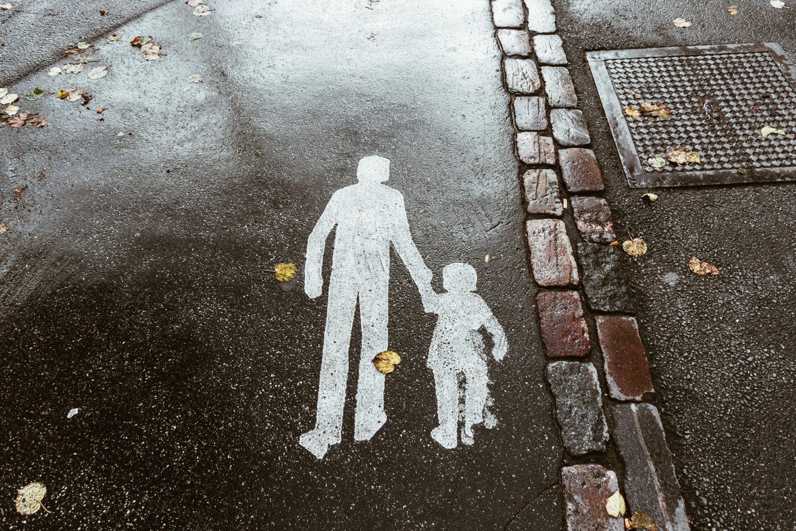 A pavement marking on wet asphalt showing an adult figure leading a child by the hand